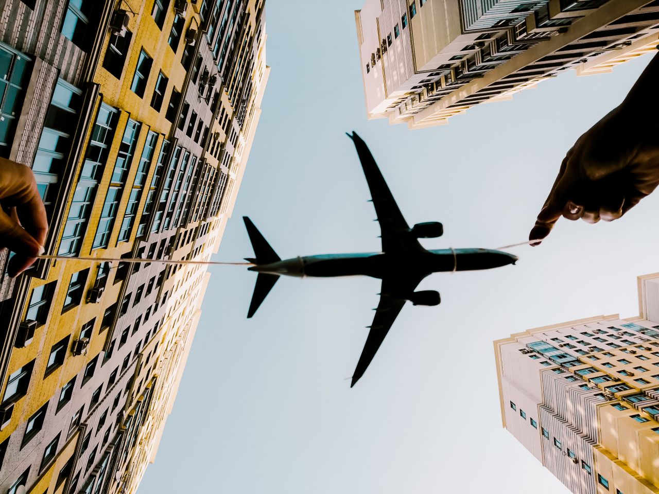 our-story A toy airplane held with string appears flying between high-rise buildings against the sky.