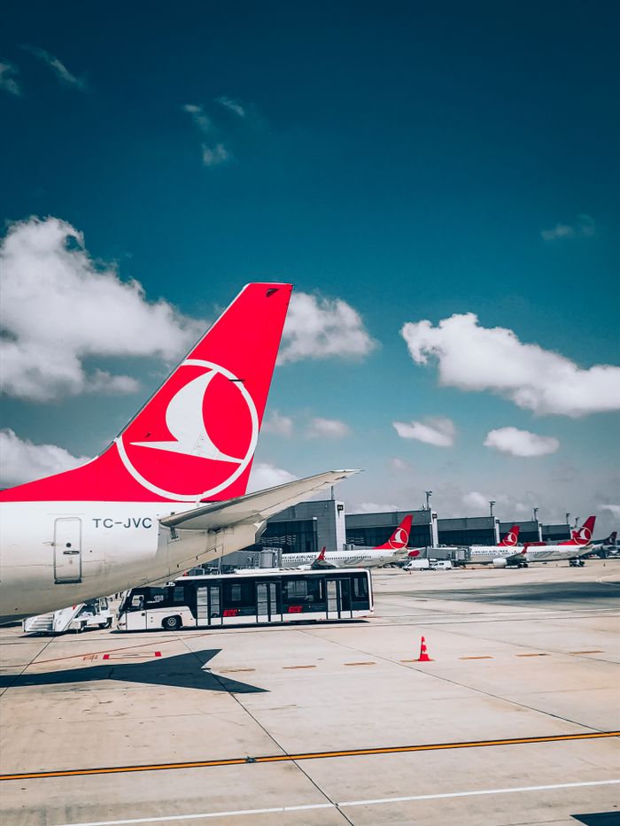 brand-01 Turkish Airlines plane tail with a busy airport background under a bright blue sky.