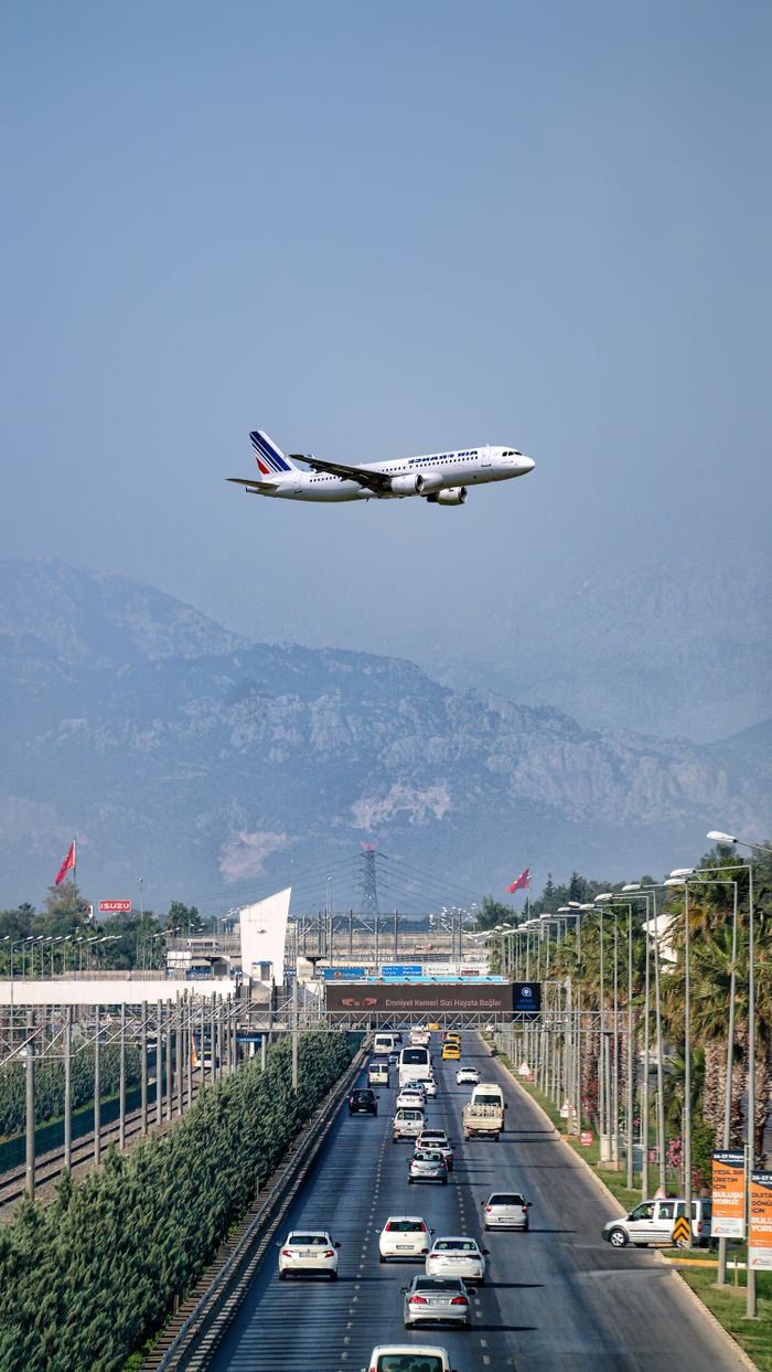 Airplane flying over a busy Antalya road with majestic mountains in the background.