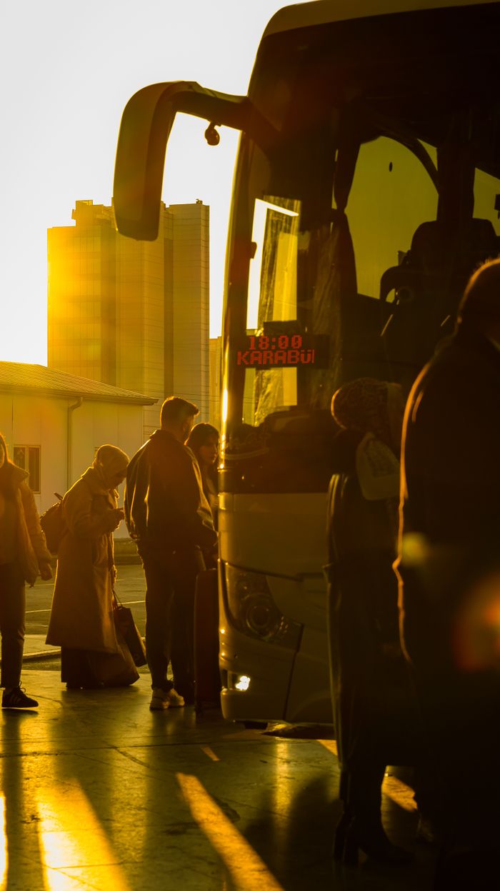 People boarding a bus in the city during sunset, creating a warm and inviting atmosphere.