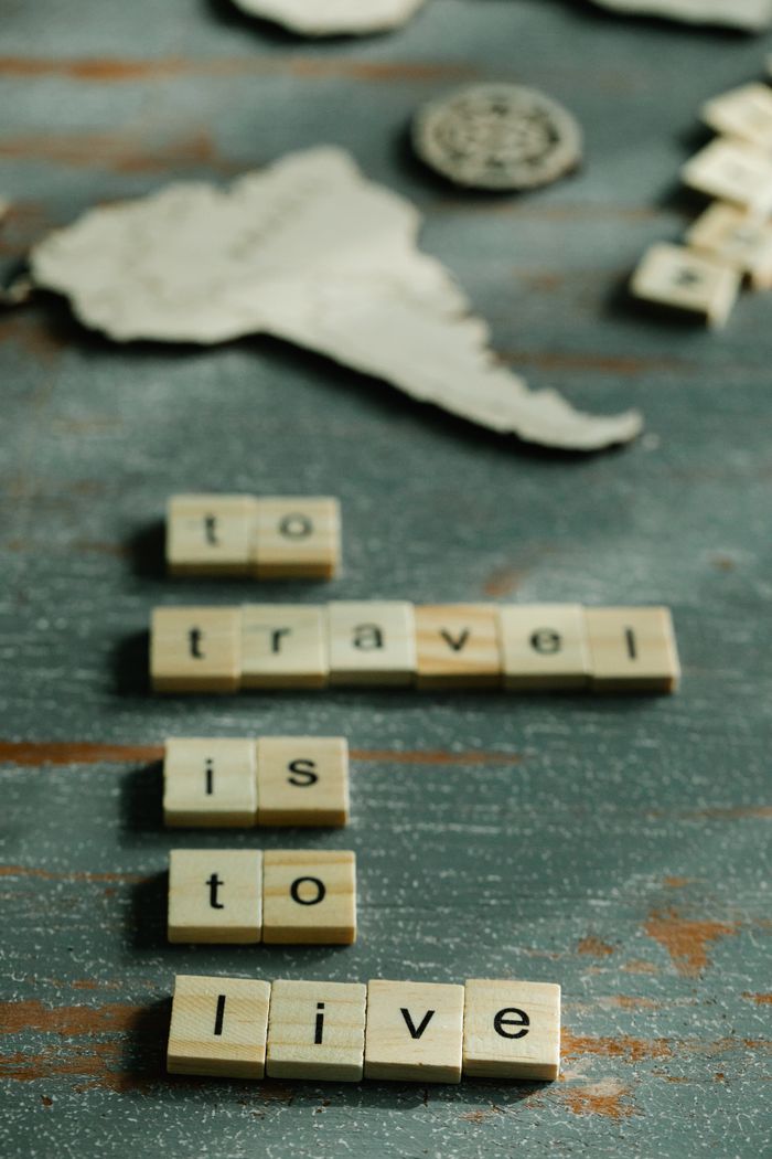 Scrabble tiles spell 'to travel is to live' on vintage map background.